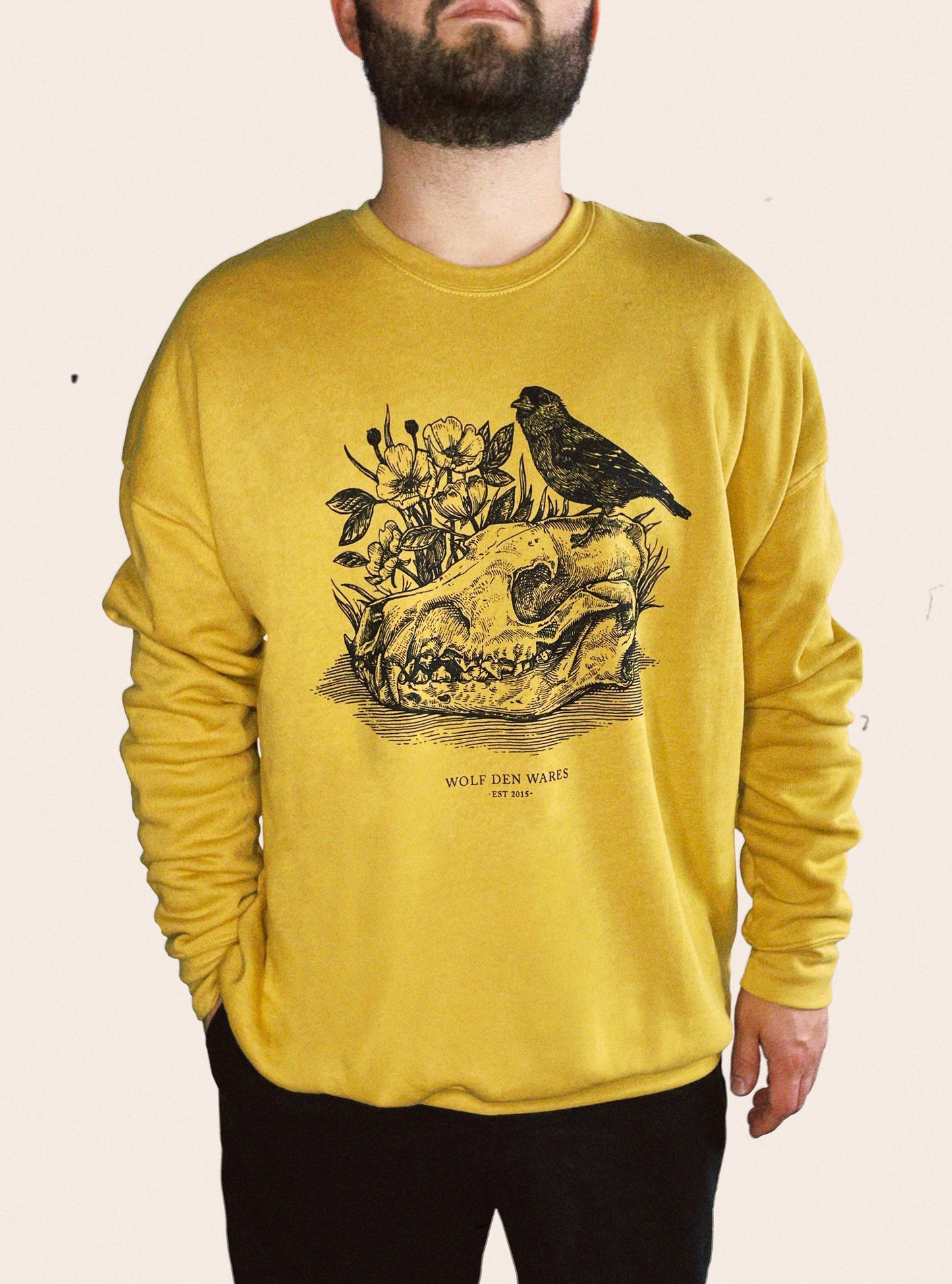 Gold Bella Canvas sponge fleece drop shoulder crew neck embellished with a wolf skull, a prairie rose, and a goldfinch and the words WOLF DEN WARES, EST 2015