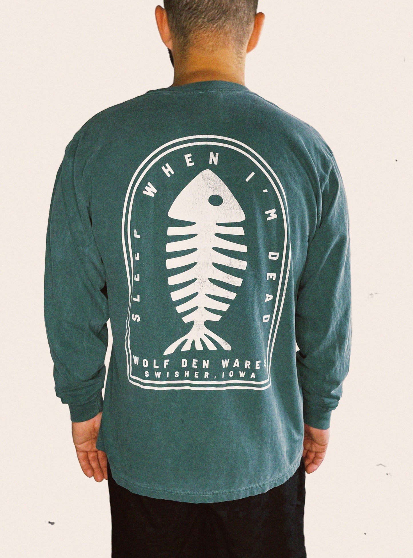 Blue spruce Comfort Colors long sleeve tee embellished with a fish skeleton logo and the words SLEEP WHEN I'M DEAD, WOLF DEN WARES, SWISHER, IOWA